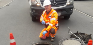 Ein Mitarbeiter von Veolia arbeitet an einem Abwasserkanal im Hintergrund steht ein weißes Fahrzeug.